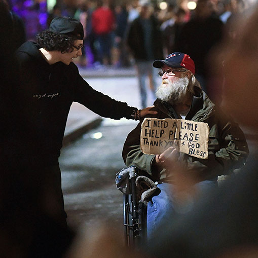 A Sixth Street reveler takes time to speak with a man in need