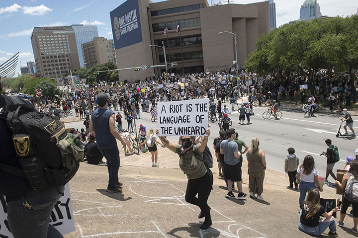 A protester holds a sign quoting Dr. Martin Luther King Jr. that says 'a riot is the language of the unheard' while climbing an Interstate 35 embankment as others gather outside police department headquarters